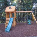 A wooden swing set with a slide and swings.